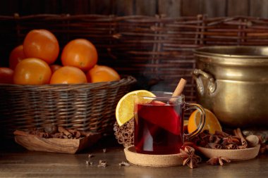 Eski ahşap bir masada malzemeli sıcak şarap. Arkaplanda portakallı pirinç tava ve sepet.
