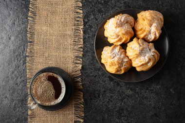 Kremalı kek ve sade kahve siyah taş bir masada. Üst görünüm.
