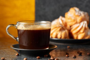 Siyah taş bir masanın üzerinde kahve çekirdekleri olan cam bardakta sade kahve. Arka plandaki kremalı keklerin içinde. Boşluğu kopyala.