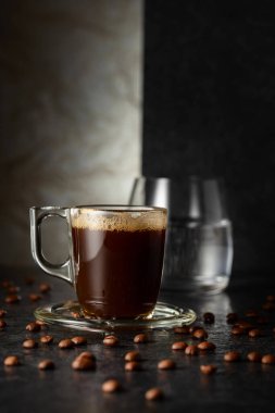 Espresso, bir bardak soğuk su ve arka planda kavrulmuş kahve çekirdekleri. Boşluğu kopyala.