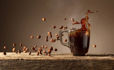 Eski ahşap bir masada cam bardakta espresso. Kavrulmuş kahve çekirdekleri hareket halinde. Boşluğu kopyala.