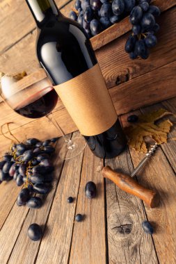 Eski ahşap bir masada bir şişe kırmızı şarap ve mavi üzüm. Eski boş bir şişede. Bir etikete odaklan.