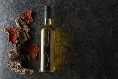 Siyah taşlı arka planda bir şişe beyaz şarap. Beyaz şarap, eski pürüzler ve kurumuş asma yaprakları. Üst Manzara. Boşluğu kopyala.