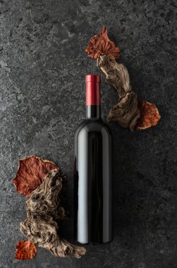 Siyah taştan bir arka planda bir şişe kırmızı şarap. Kırmızı şarap, eski pürüzler ve kurumuş asma yaprakları. Üst Manzara. Boşluğu kopyala.
