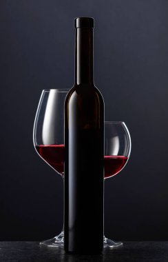 Siyah arka planda kırmızı şarap şişesi ve bardakları..