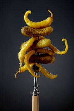 Çatalın üzerinde sebze turşusu. Siyah arka planda konserve sarı biber ve salatalık..