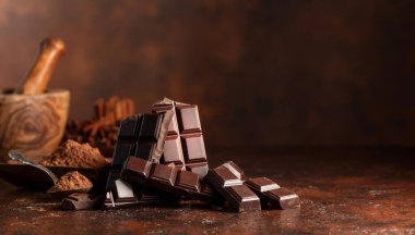 Kahverengi bir masada kırılmış siyah çikolata ve kakao tozu. Boşluğu kopyala.