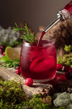 Eski ahşap bir tahtada buzlu, limonlu ve biberiyeli kızılcık kokteyli. İçki buzlu bir bardağa dökülür..