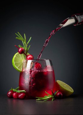 Böğürtlen, limon ve biberiyeyle süslenmiş yabanmersini kokteyli. Buzlu dondurulmuş bardakta kızılcık likörü dökülüyor. Boşluğu kopyala.