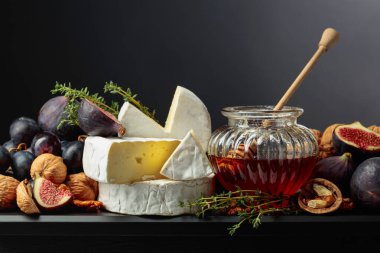 İncirli, üzümlü, cevizli, ballı ve kekikli Camembert peyniri. Siyah arka planda meyveli yumuşak peynir..