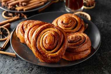 Kanelbullar - İsveç tarçınlı çörekler ya da dürümler. Siyah taş bir masada taze pişmiş çörekler..