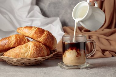 Freshly baked croissants and coffee with cream. Pouring creme in a glass cup of coffee.