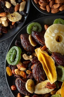 Kurutulmuş tropikal meyve, fındık ve kuru üzümler siyah bir taş masada. Üst görünüm.