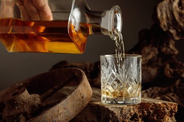 Glass of whiskey on a wooden board. Whiskey is poured from a decanter into a glass. Vintage background with old wood and rusty metal. Concept of old expensive drinks. clipart