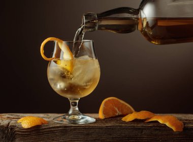 Eski moda bir kokteyl, buz ve portakal kabuğu ile eski bir ahşap masa. Viski şişeden doğal buzla bardağa dökülür..