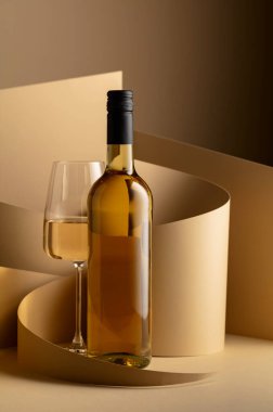 Bottle and glass of white wine on a beige background. Copy space.