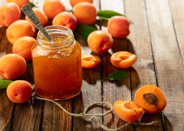 Cam kavanozda kayısı reçeli ve eski ahşap bir masada taze meyve..