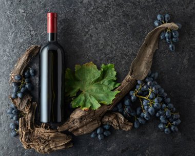 Bir şişe kırmızı şarap, mavi üzüm ve siyah taşlı arka planda eski asma parçaları. Üst Manzara. Boşluğu kopyala.