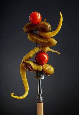 Çatalın üzerinde sebze turşusu. Siyah arka planda konserve sarı biber, salatalık ve domates..