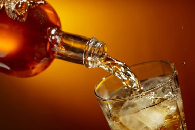 Buzlu bir bardağa dökülen bir şişe viski. Sıvı akış, canlı turuncu arka planda yakın plan görüntüsü yakalamış. Boşluğu kopyala.