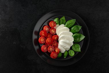 Siyah taşlı arka planda fesleğen ve kiraz domatesli Mozzarella. Kopyalama alanı olan üst görünüm.