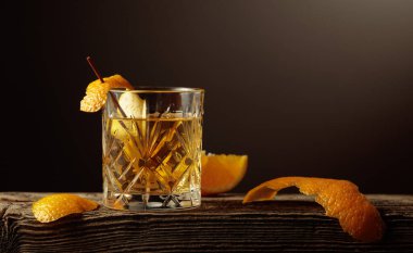 Eski ahşap bir tahtanın üzerinde portakal kabuğu olan kısa kristal bardakta zengin bir Old Fashioned kokteyli. Boşluğu kopyala.
