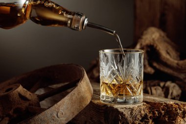 Eski bir tahta üzerinde bir bardak viski. Viski şişeden bardağa dökülür. Eski ahşap ve paslı metalle klasik arka plan. Eski pahalı içecekler kavramı.
