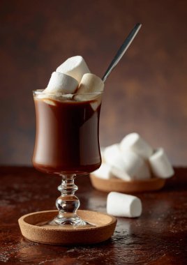 Eski kahverengi bir masanın üzerindeki cam bardakta kremalı sıcak çikolata. Boşluğu kopyala.