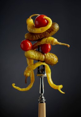 Çatalın üzerinde sebze turşusu. Siyah arka planda konserve sarı biber, salatalık ve domates..