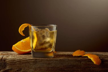 Kısa bardakta zengin bir Old Fashioned kokteyli, buzlu koyu kehribar likörü, eski ahşap bir tahtanın üzerinde portakal kabuğu ile süslenmiş. Boşluğu kopyala.