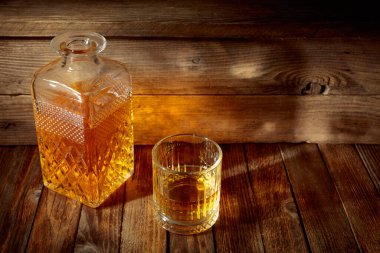 Zarif viski bardağı ve kehribar sıvısıyla dolu sürahi eski bir ahşap masada. Boşluğu kopyala.
