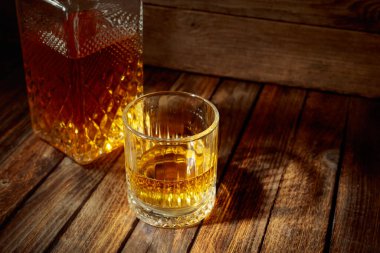 Zarif viski bardağı ve kehribar sıvısıyla dolu sürahi eski bir ahşap masada. Boşluğu kopyala.