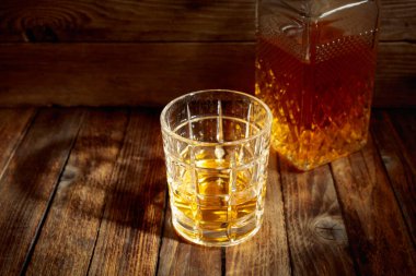 Zarif viski bardağı ve kehribar sıvısıyla dolu sürahi eski bir ahşap masada. Boşluğu kopyala.