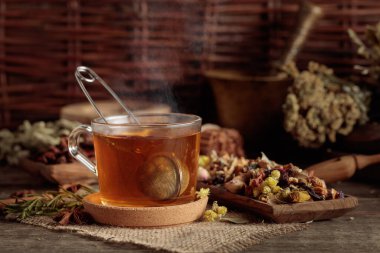 Eski ahşap bir masada çeşitli kurutulmuş bitkilerle, çiçeklerle ve baharatlarla bir fincan bitki çayı. Bitkisel ilaç kavramı.