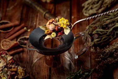 Çeşitli kurutulmuş otlar ve baharatlar cam bir çaydanlığa dökülüyor. Aromaterapi ya da bitkisel tıp konsepti.