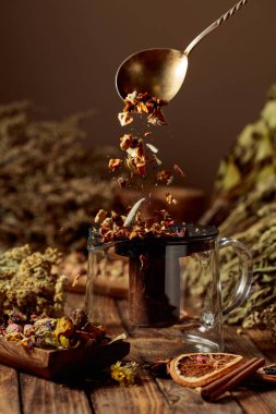 Çeşitli kurutulmuş otlar ve baharatlar cam bir çaydanlığa dökülüyor. Aromaterapi ya da bitkisel tıp konsepti.