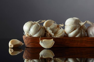 Siyah yansıtıcı arka planda ahşap kaptaki sarımsak soğanları. Boşluğu kopyala.