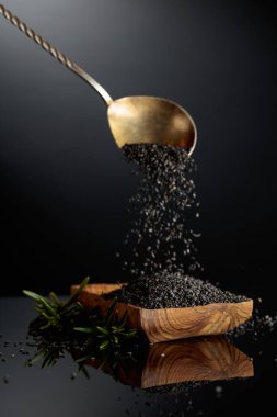 Siyah yansıtıcı arka planda siyah susam. Susam ağaçtan bir kaseye dökülür..