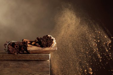 Tarçın çubukları eski ahşap bir masada. Tarçın tozu patlaması. Boşluğu kopyala.