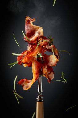 Çatalda kızarmış pastırma, siyah arka planda biberiye serpiştirilmiş..