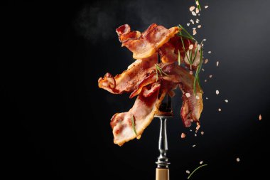 Çatalda kızarmış pastırma, biberiye ve pembe tuz serpiştirilmiş, siyah arka planda fotokopi alanı olan..