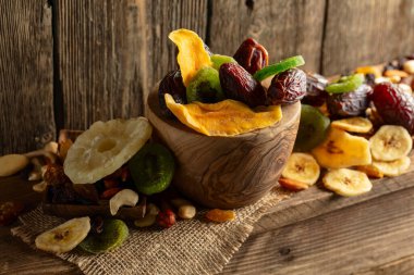 Kurumuş tropikal meyveler, çeşitli fındıklar ve kuru üzümler eski ahşap bir masada..