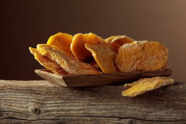 Kahverengi arka planda ahşap bir tabakta kurutulmuş mango dilimleri. Boşluğu kopyala.