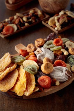 Kurutulmuş mango dilimleri, tropikal meyveler, fındıklar ve kuru üzümler eski ahşap bir masada..