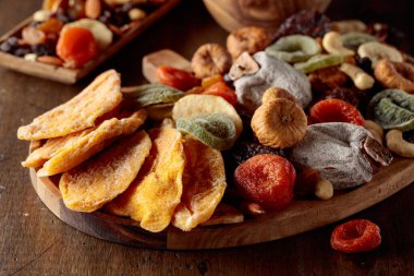 Kurutulmuş mango dilimleri, tropikal meyveler, fındıklar ve kuru üzümler eski ahşap bir masada..