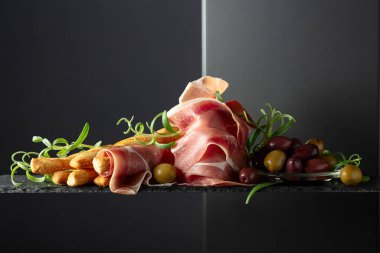 Siyah arka planda ekmek çubuğu, zeytin ve biberiyeli jambon. Geleneksel İtalyan atıştırmaları.