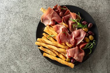 Siyah tabakta ekmek çubuğu, zeytin ve biberiyeli jambon. Geleneksel İtalyan atıştırmalıkları. Üst görünüm.