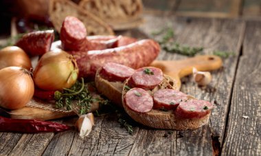 Kurutulmuş sosis, kekik, soğan, sarımsak ve biber. Eski ahşap bir masada sosis ve baharat..