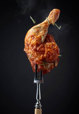 Siyah arka planda biberiye serpilmiş ızgara tavuk budu. Çataldaki tavuk budu..