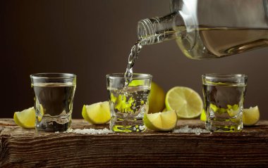 Eski ahşap bir tahtanın üzerinde tuz ve limon dilimli altın tekila. Tekila şişeden bardağa dökülür..